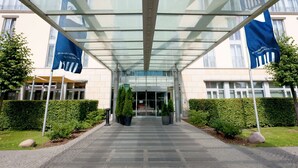 A modern building entrance with a glass canopy, a paved pathway, and flags on either side. - Dorint Hotel Potsdam (Potsdam)
