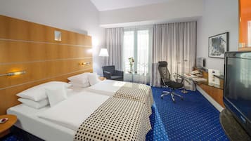 A hotel room with a large bed, a desk, a chair, a TV, and a window with curtains.