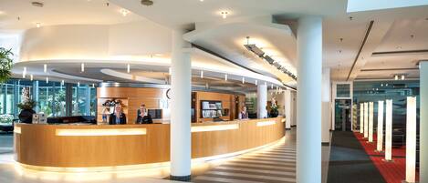 A modern hotel lobby with a curved reception desk, large columns, and a check-in area.