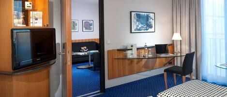 A hotel room with a bed, a desk with a computer, a TV, a chair, and a window with curtains.