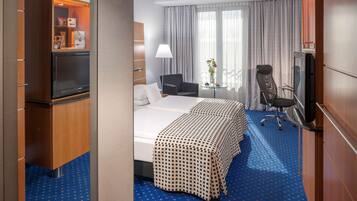 Une chambre d’hôtel comprenant un lit, deux chaises, une télévision, un bureau et un minibar.
