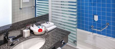 A modern bathroom with a granite countertop, a white sink, a bathtub, and blue-tiled walls.