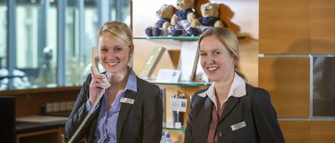 Two receptionists at a hotel desk with a glass display case containing teddy bears.