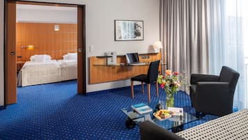 Une chambre d’hôtel avec un lit, un bureau, une chaise et une table basse en verre sur laquelle se trouvent un livre et des fruits.