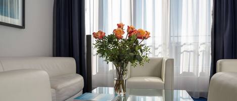 A modern hotel room with a glass coffee table, a vase of flowers, a book, and a sofa.