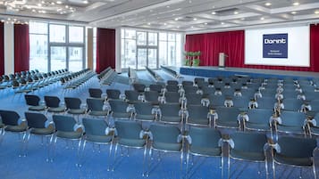 A conference room with rows of chairs, a stage with a screen, and large windows.