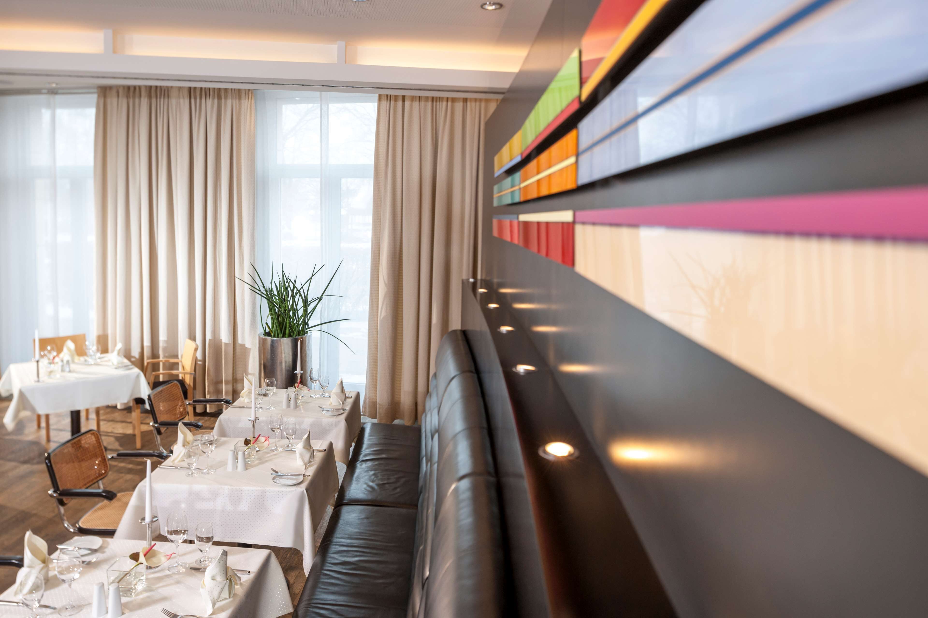 A modern dining area with tables set for a meal, a sofa, and a large window with curtains.