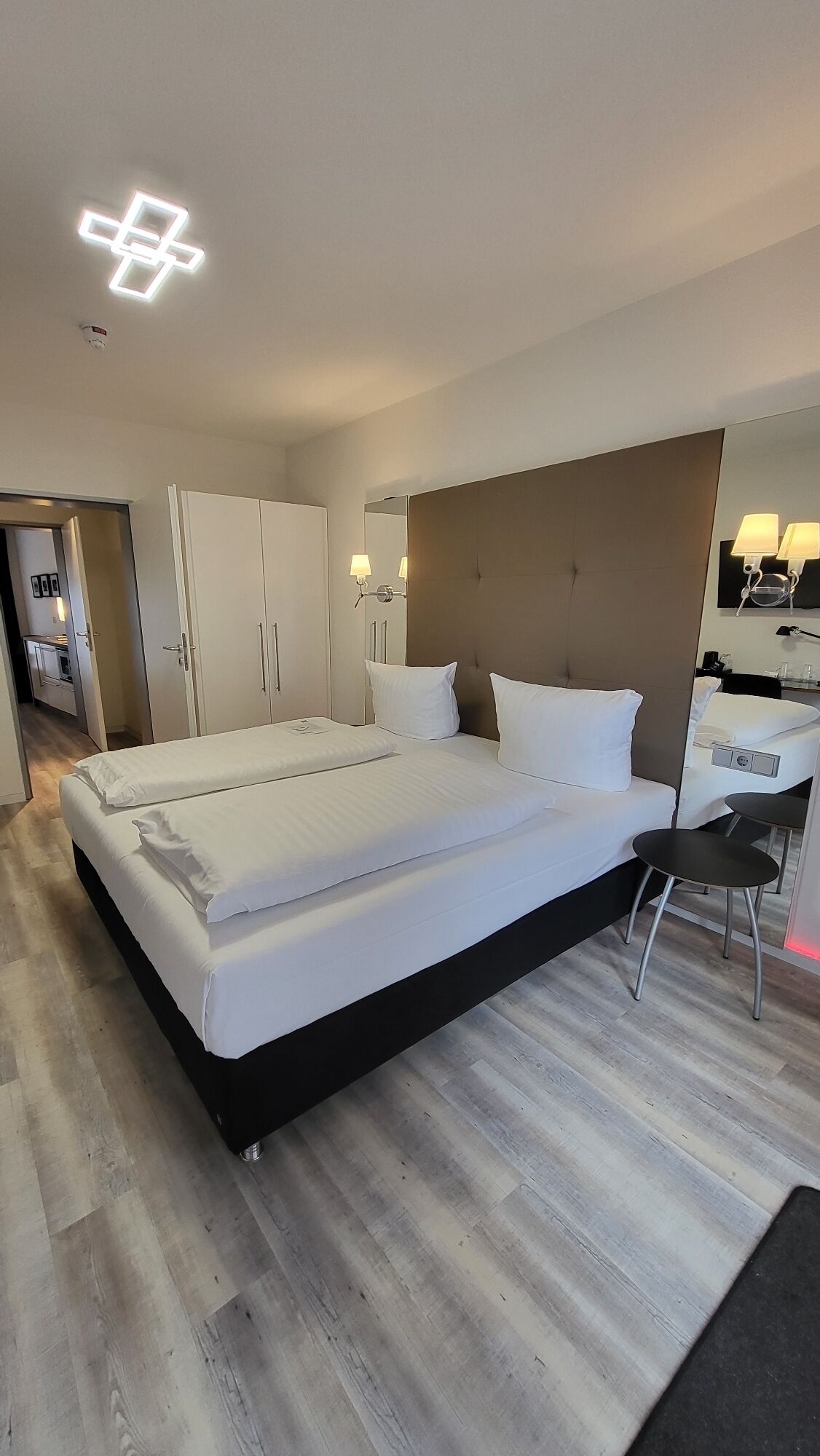 A modern hotel room with a large bed, a desk, and a mirror.