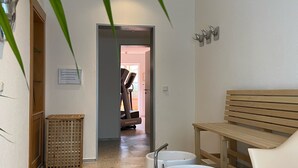 A hallway with a wooden bench, two white sinks, a trash bin, and a door leading to another room. - Hotel Amadeus (Hannover)