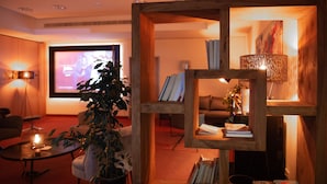 A cozy living room with a television, a coffee table, a sofa, and a wooden bookshelf. - Hotel Amadeus (Hannover)