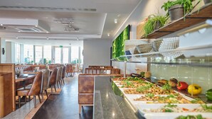 A buffet area with various food options, a seating area with chairs, and a wall with greenery. - Hotel Amadeus (Hannover)
