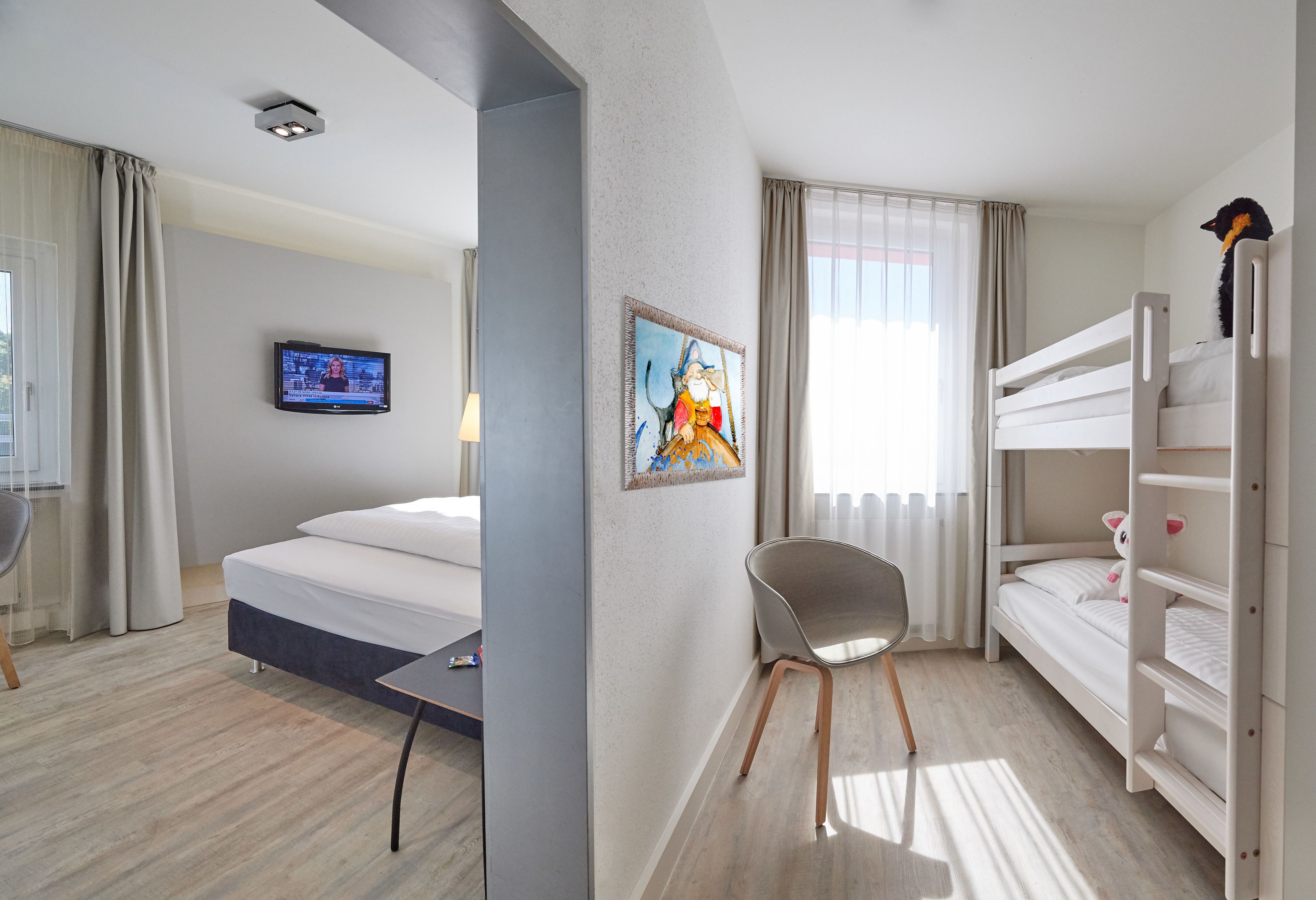 Ein Hotelzimmer mit Bett, Schreibtisch, Stuhl, Stockbett, Fernseher und einem Bild an der Wand.