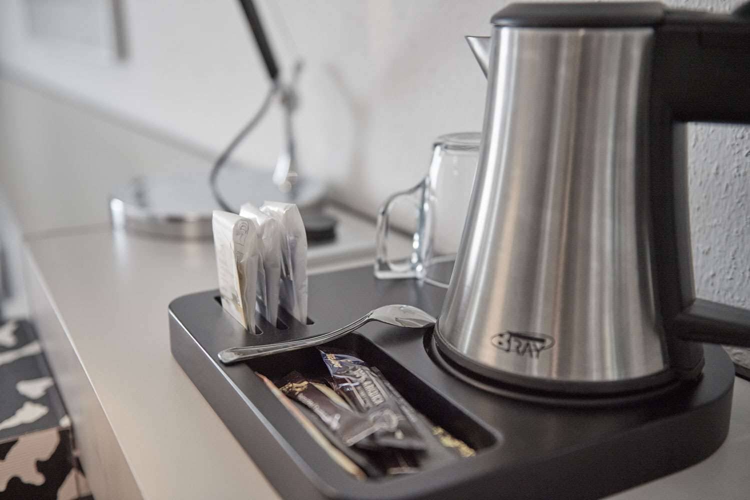 A coffee machine with a tray, a glass, and a kettle on a countertop.