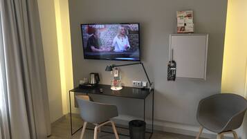 Une chambre d’hôtel équipée d’un téléviseur fixé au mur, d’un bureau avec une lampe, de deux chaises, d’une poubelle et d’un mini-bar.