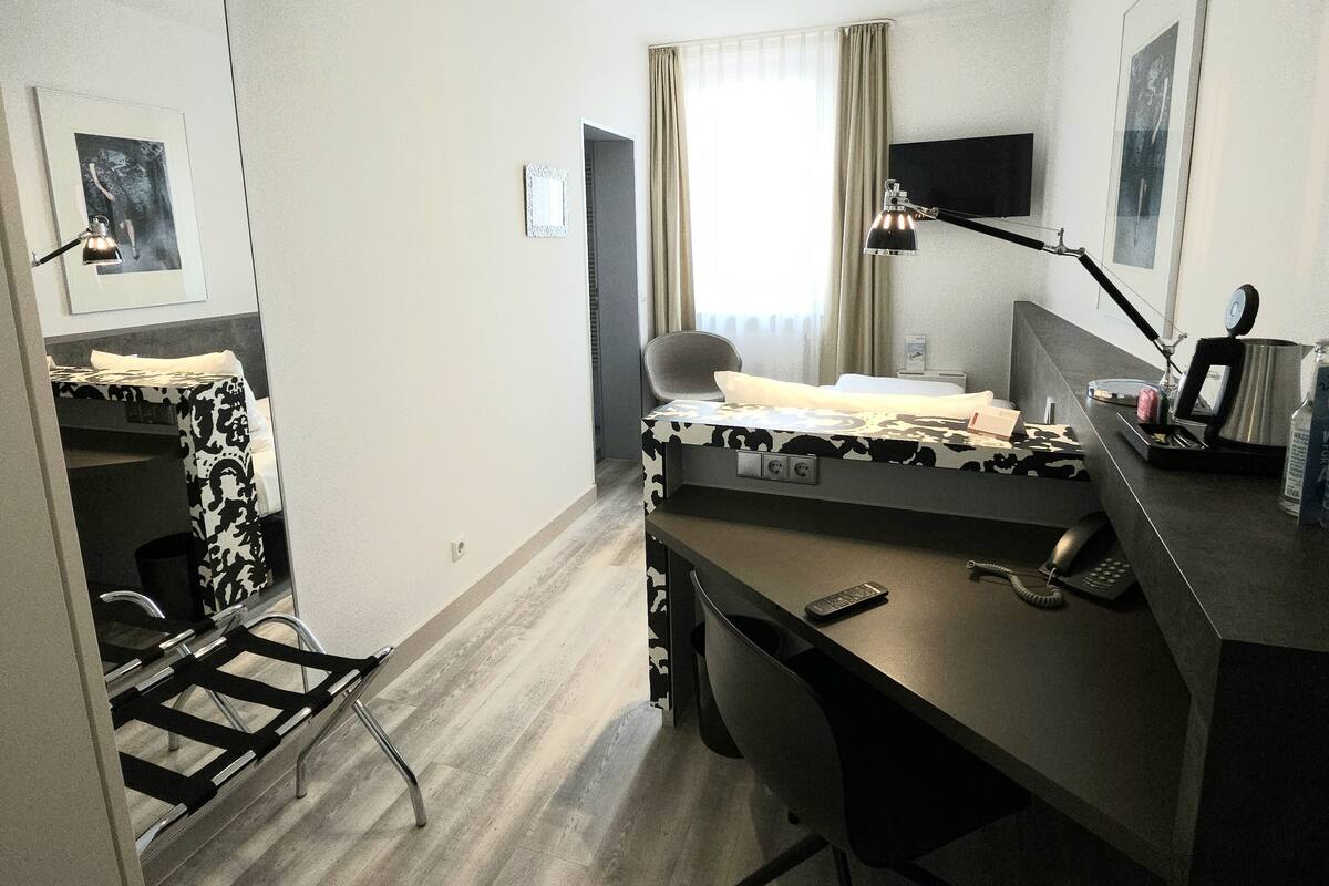 A compact hotel room with a bed, desk, chair, and a small kitchenette area.
