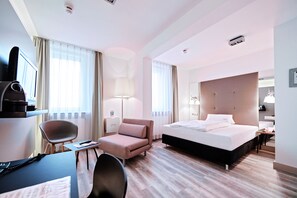 A hotel room with a bed, a desk, a chair, a lamp, and a television. - Hotel Amadeus (Hannover)