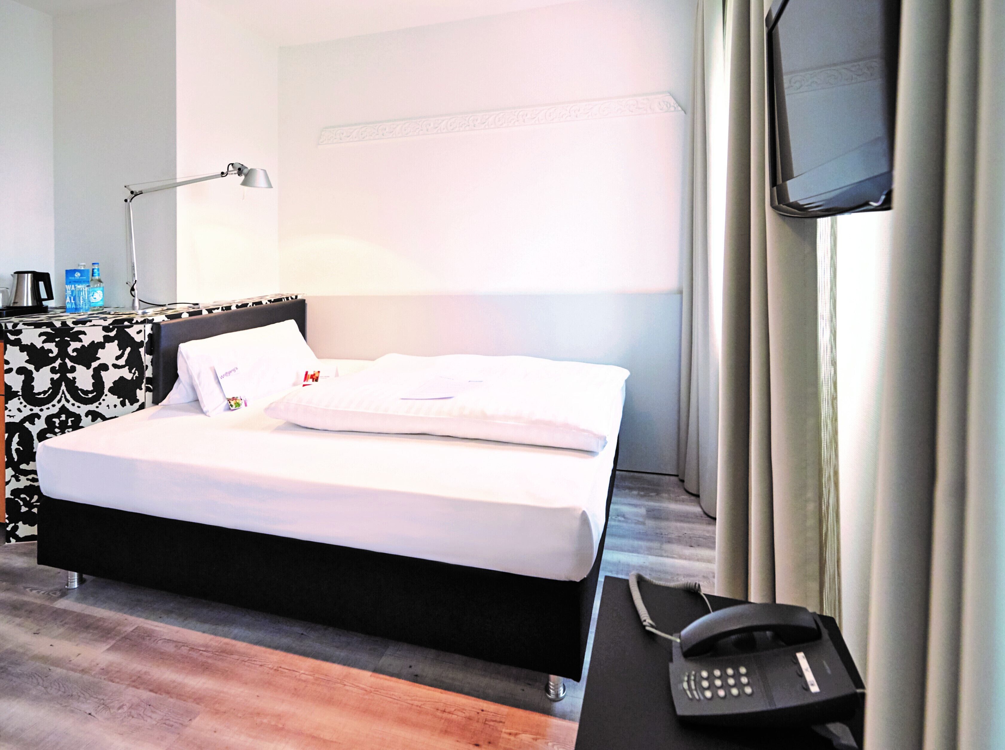 Ein Hotelzimmer mit Bett, Nachttisch, Lampe und Telefon.