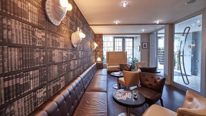 A modern lounge area with leather seating, a patterned wall, and a large window. - Hotel Amadeus (Hannover)