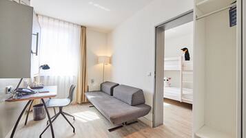 Ein moderner, gut beleuchteter Raum mit Schreibtisch, Stuhl, Sofa und einer kleinen Ecke für Haustiere.