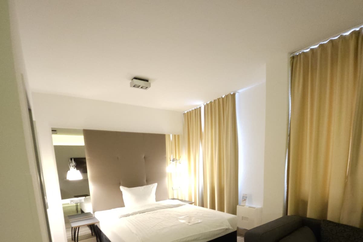 A modern hotel room with a bed, a sofa, a desk, and a mirror.