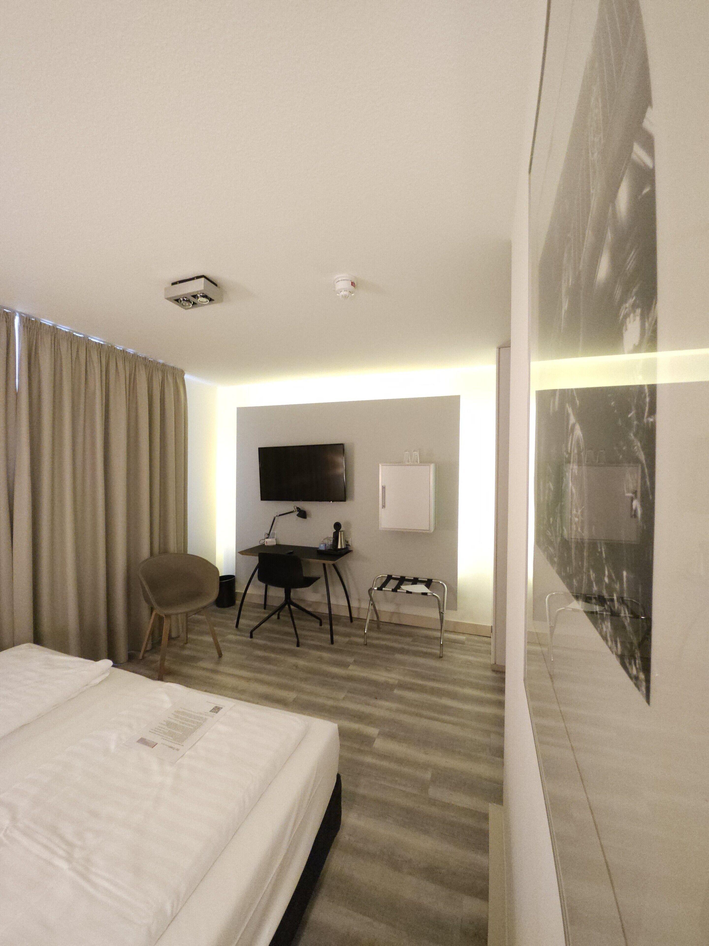 Een hotelkamer met een bed, een bureau met stoel, een televisie en een groot poster aan de muur.