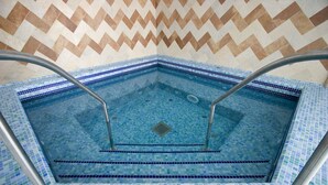Una piscina rectangular con mosaicos azules y barandillas de metal.