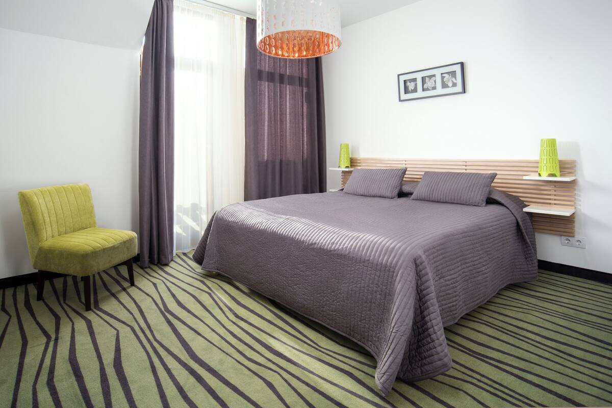 A hotel room with a bed, a chair, a nightstand, and a picture on the wall.