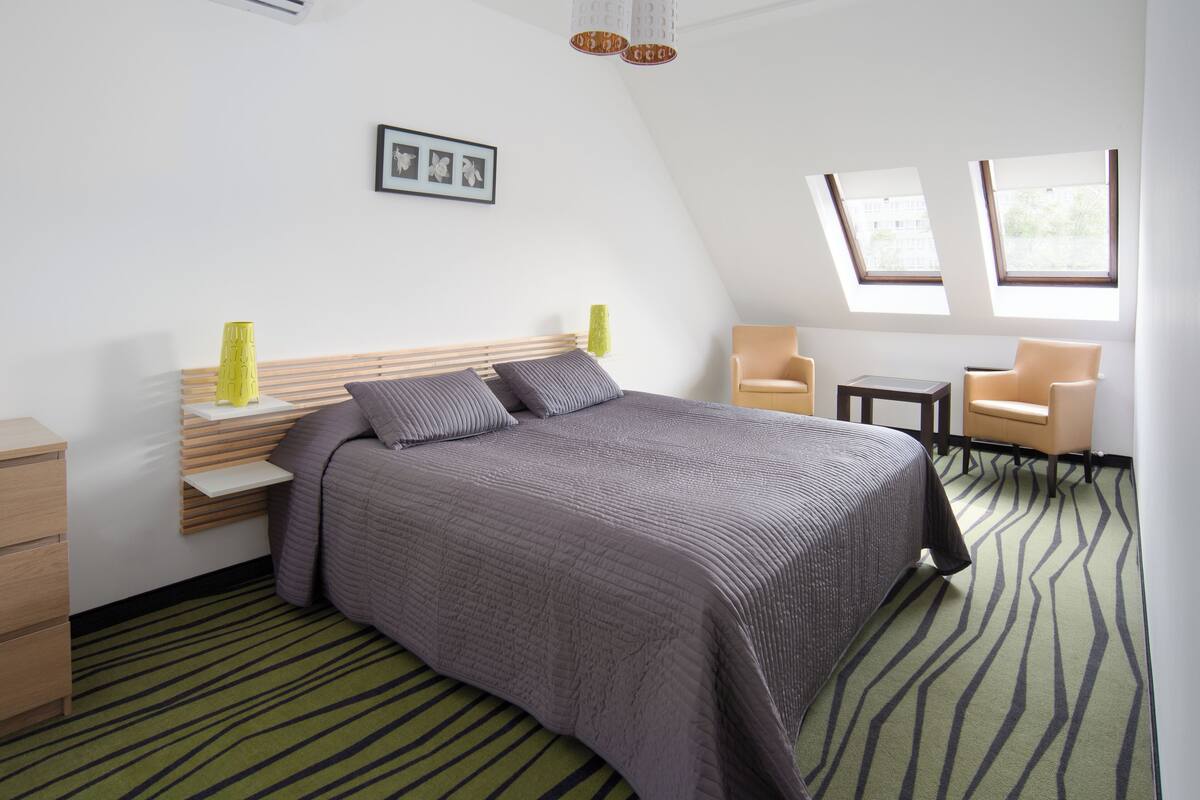 A modern bedroom with a bed, two chairs, a small table, and a picture on the wall.
