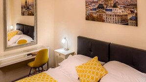 A hotel room with a bed, a desk, a chair, a nightstand with a lamp, and a large mirror. - Bobbio Hotel (Budapest)