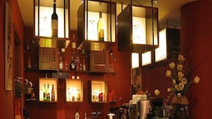 A bar area with multiple illuminated shelves displaying bottles, a counter with various items, and a vase with flowers. - Bobbio Hotel (Budapest)