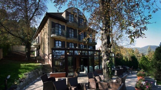 A building with a glass conservatory, outdoor seating, and a view of the mountains. - Bobbio Hotel (Budapest)
