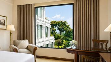 A hotel room with a large window, a bed, a chair, a desk, and a lamp.