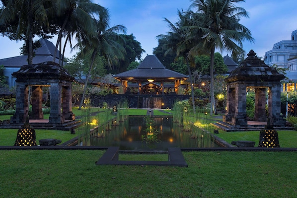 A serene garden with a central pond, stone gazebos, and a traditional building with a tiled roof. - Hyatt Regency Yogyakarta (Ngaglik)
