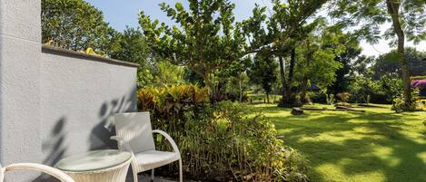 Un patio con due poltrone in vimini, un muro in pietra e un prato ben curato con alberi e siepi.