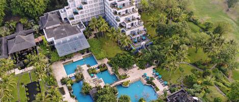 Vista aérea de un complejo turístico con varias edificaciones, una amplia piscina y exuberante vegetación.