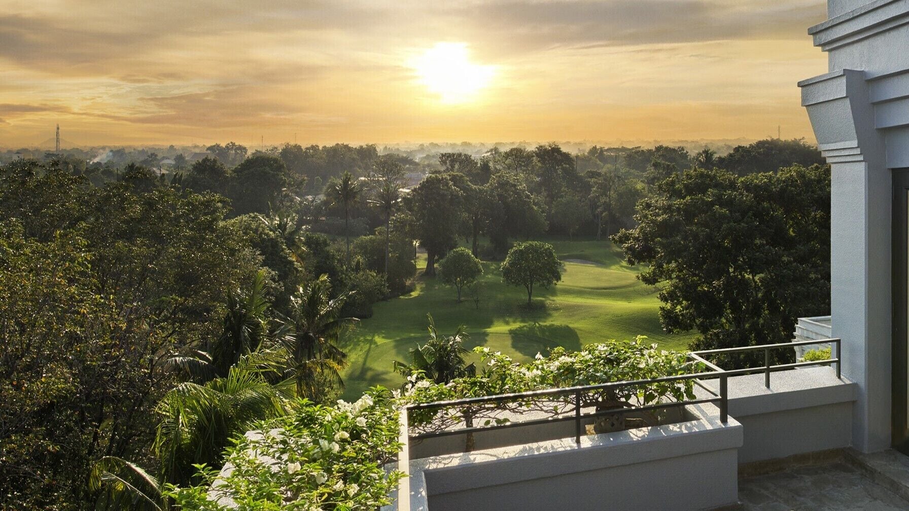 A view of a golf course with a clear sky and sunlight, surrounded by lush greenery.