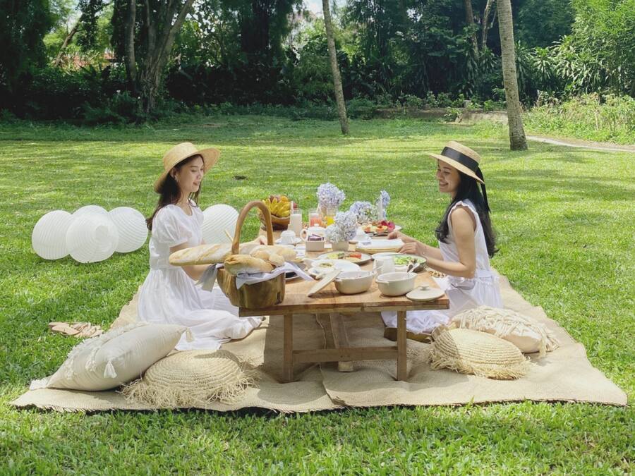 Un montaje para picnic en un césped, con una mesa de madera, comida y bebidas.