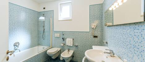 A bathroom with a bathtub, two toilets, a bidet, a sink, and a mirror with lights.