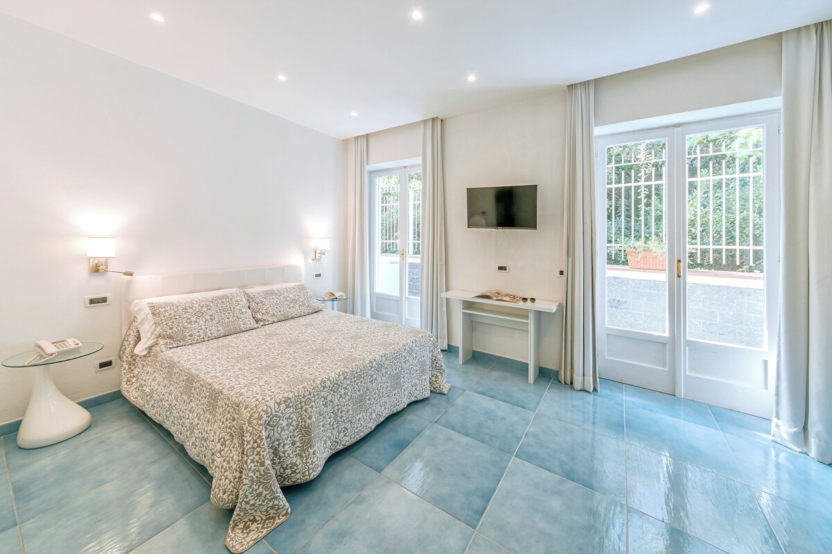 A bedroom with a bed, a TV, a desk, and a window with curtains.
