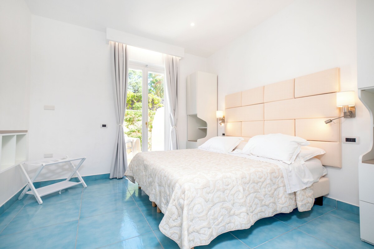 Een slaapkamer met een bed, nachtkastje, stoel en uitzicht op de omgeving.