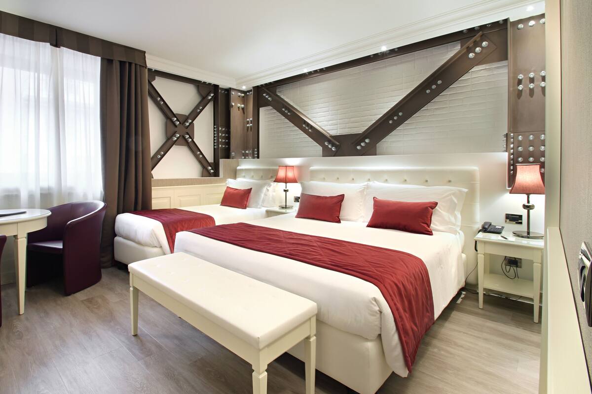 Habitación de hotel con dos camas, un escritorio, una silla y un banco.