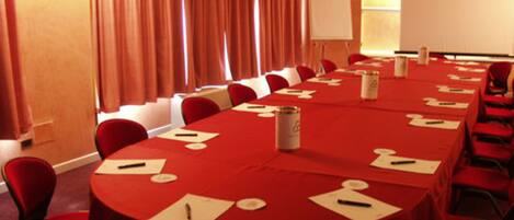 A conference room with a long table, red chairs, and a whiteboard.