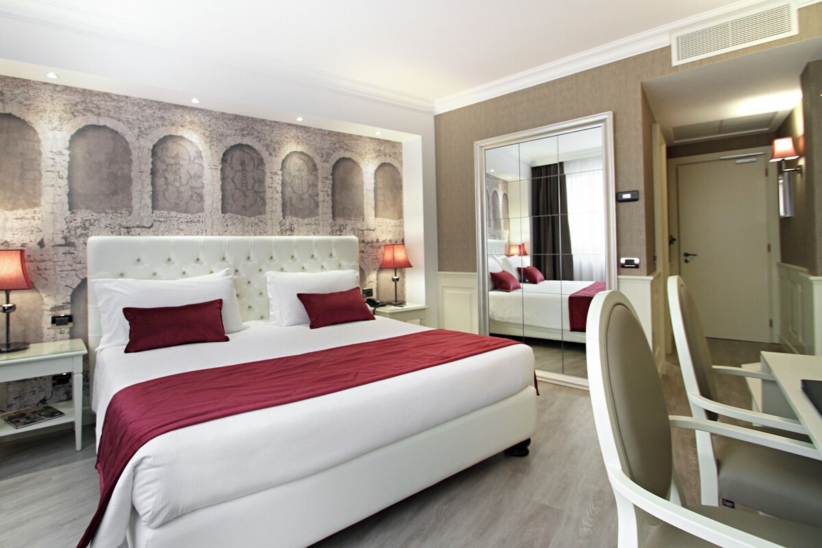 Een hotelkamer met een groot bed, twee nachtkastjes met lampen, een spiegel en een wand met bakstenen motief.