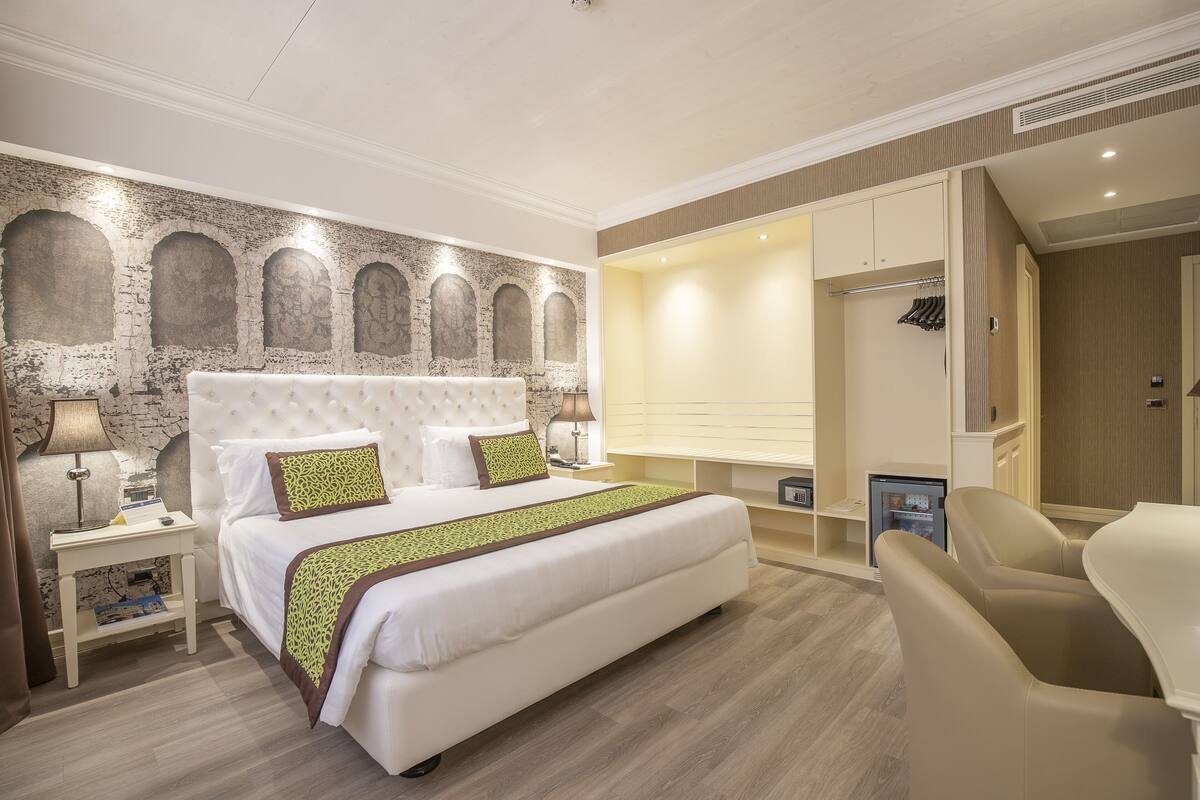 Habitación de hotel con una cama grande, una mesita de noche con lámpara, un rincón de descanso con una silla y un armario.