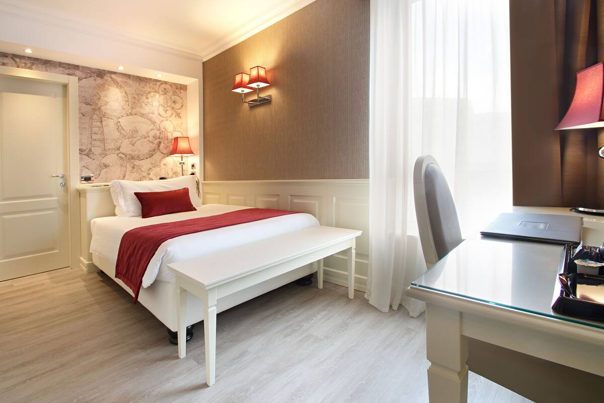 Una habitación de hotel con cama, escritorio, silla y lámpara.