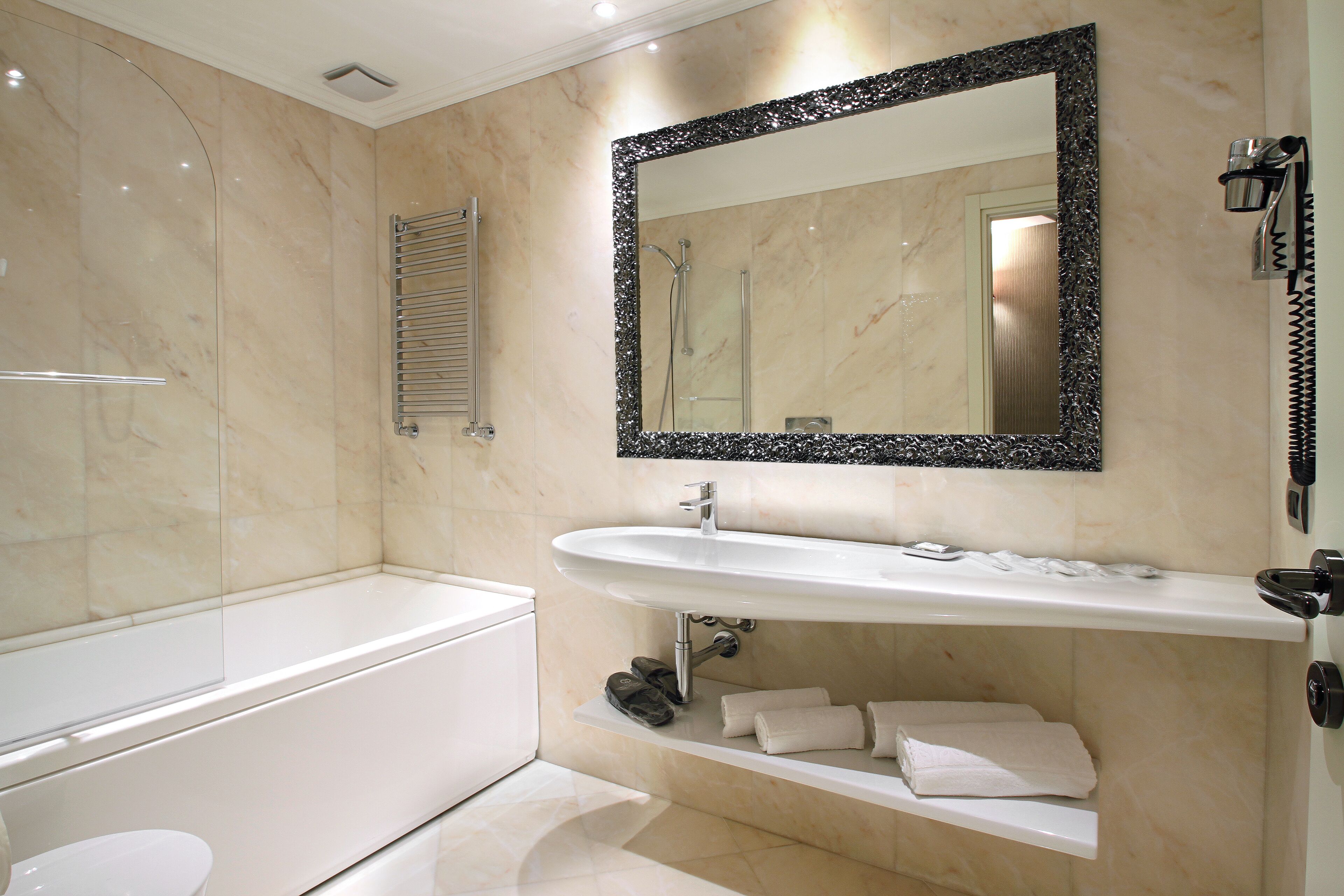 A modern bathroom with a large mirror, white sink, and a bathtub.