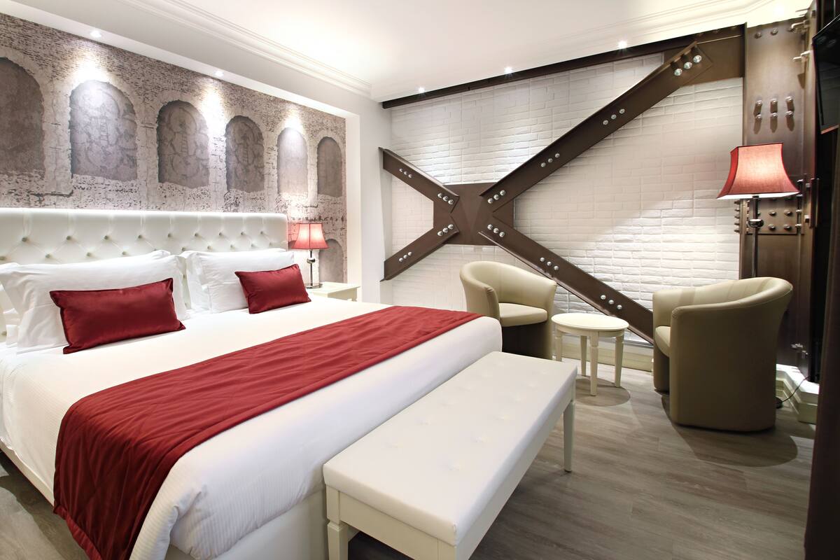 Una habitación de hotel moderna con una cama grande, un banco, dos sillones y un diseño de pared con forma de estrella.
