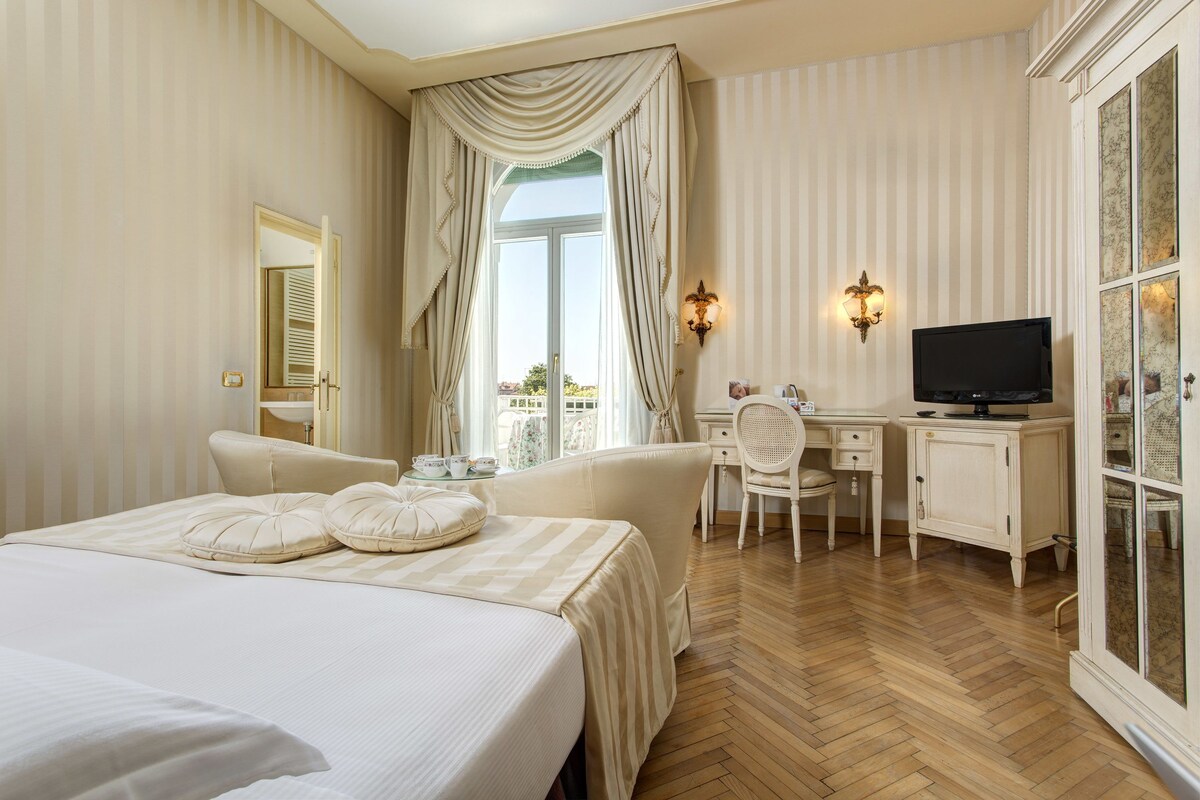 A hotel room with a large bed, a desk, a television, and a wardrobe.