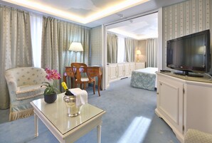 Una camera d'albergo con un divano, un tavolo con una bottiglia e fiori, una televisione e un letto.