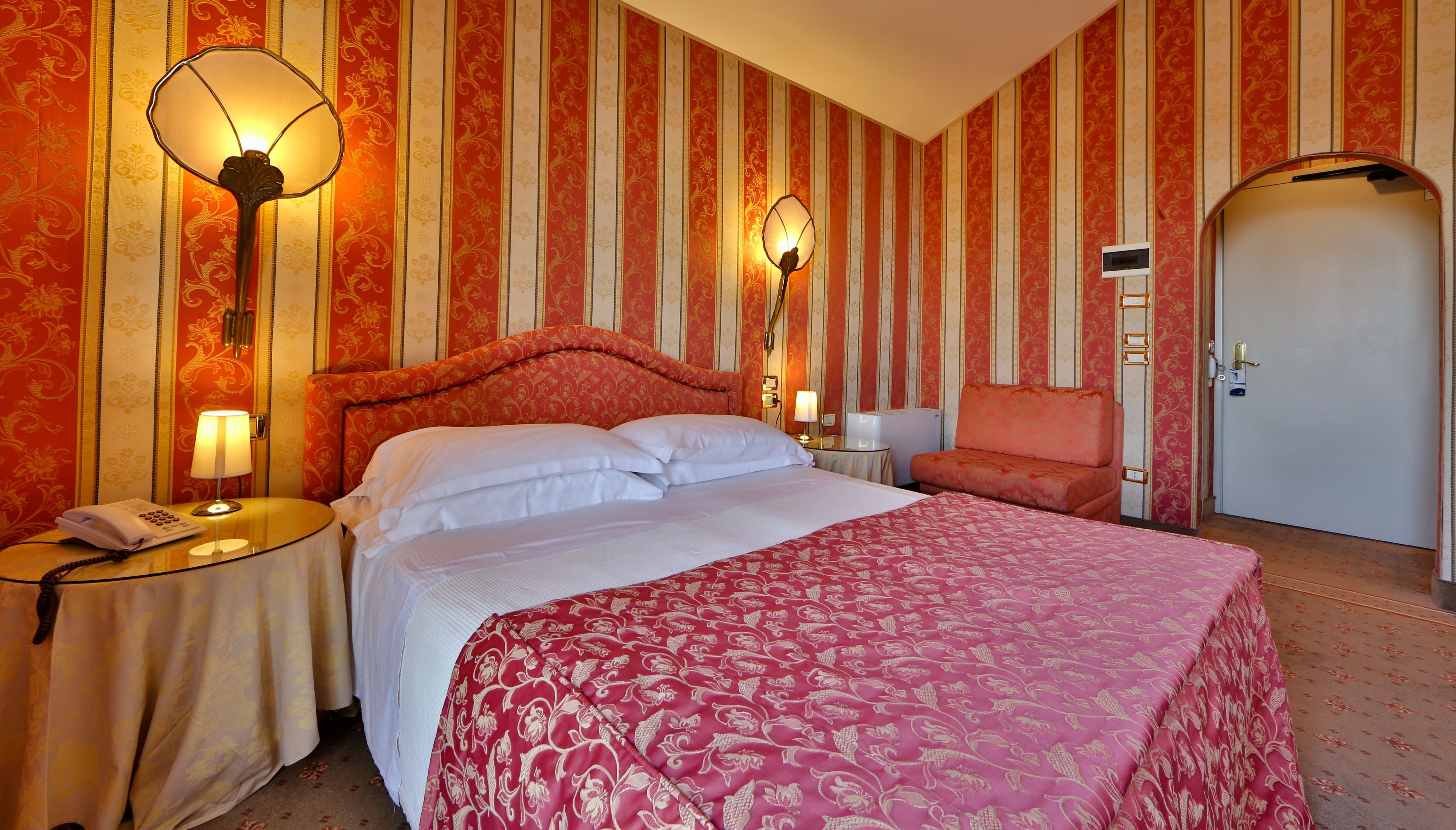 A hotel room with a large bed, two bedside lamps, a telephone, and a door with a handle.